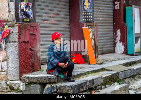 Eine ältere chinesische Frau blickt nachdenklich, als Sie über einige Stufen in der antiken Stadt Daxu, China sitzt. Stockfoto