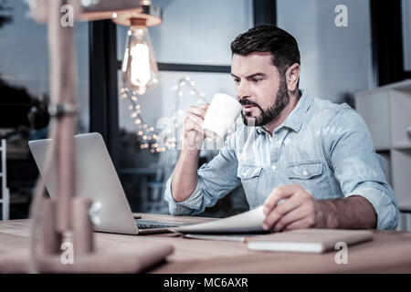 Konzentriert verantwortlichen Mann Tee trinken und auf Laptops. Stockfoto
