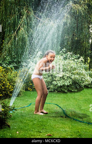 Junge Mädchen Spaß haben, während sie unter Garten Brunnen im heißen Sommer Tag stehen. Stockfoto