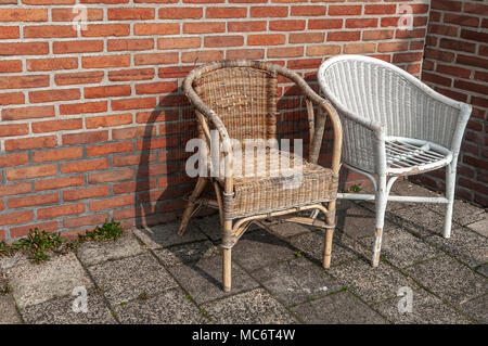 Zwei verschlissene Korbstühlen vor einer Mauer aus Stein platziert Stockfoto