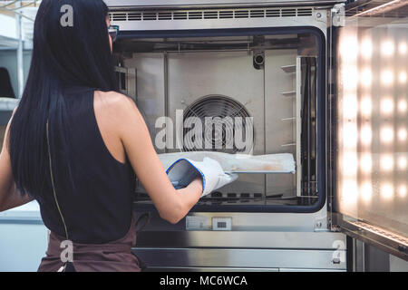 Mädchen Baker zieht aus dem Ofen frisch gebackene Backwaren aus dem Ofen. Stockfoto