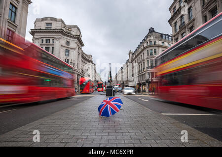 London, England - British Regenschirm bei Beschäftigten der Regent Street mit kultigen roten Doppeldeckerbussen unterwegs Stockfoto