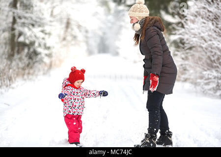 Junge schöne Mädchen mit Hut wihite posiert vor einem Winter Park Hintergrund und spielen mit den süßen Mädchen mit dem Schnee im Wald Stockfoto