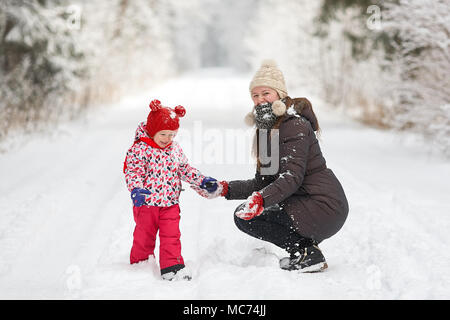 Junge schöne Mädchen mit Hut wihite posiert vor einem Winter Park Hintergrund und spielen mit den süßen Mädchen mit dem Schnee im Wald Stockfoto