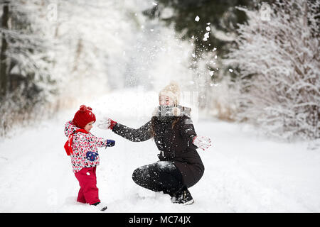 Junge schöne Mädchen mit Hut wihite posiert vor einem Winter Park Hintergrund und spielen mit den süßen Mädchen mit dem Schnee im Wald Stockfoto