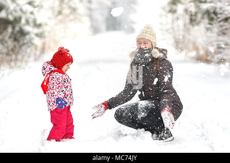 Junge schöne Mädchen mit Hut wihite posiert vor einem Winter Park Hintergrund und spielen mit den süßen Mädchen mit dem Schnee im Wald Stockfoto