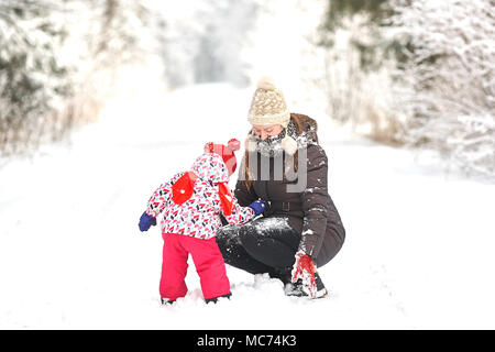 Junge schöne Mädchen mit Hut wihite posiert vor einem Winter Park Hintergrund und spielen mit den süßen Mädchen mit dem Schnee im Wald Stockfoto