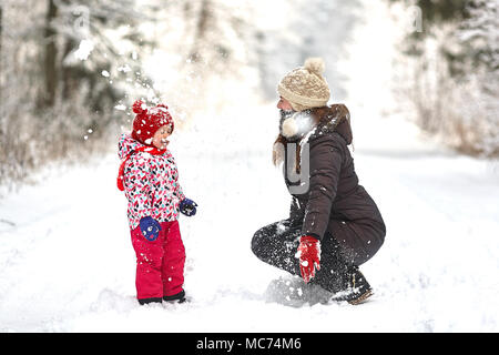 Junge schöne Mädchen mit Hut wihite posiert vor einem Winter Park Hintergrund und spielen mit den süßen Mädchen mit dem Schnee im Wald Stockfoto