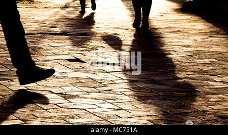 Blurry Beine Silhouetten und Schatten von Menschen zu Fuß auf Stadt gemusterten Platz im Sonnenuntergang Stockfoto