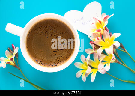 Eine Tasse Kaffee mit bunten Blumen und guten Morgen Hinweis auf der blauen Fläche. Stockfoto