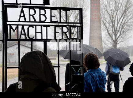 13 April 2018, Deutschland, Oranienburg: Eine Gruppe von Besuchern durch das Tor gehen, im ehemaligen Konzentrationslager mit der Aufschrift "Arbeit macht frei" (Lit. Arbeit macht frei. Eine neue Ausstellung in Sachsenhausen ist die Erinnerung an die Ereignisse, die sich im Jahr 1938, nahm, mit der Progromnacht (Nacht von Glasscherben, war ein Höhepunkt der Verfolgung der Juden. Foto: Bernd Settnik/dpa-Zentralbild/dpa Stockfoto