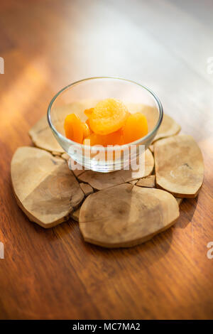 Getrocknete Aprikosen in eine Glasschüssel auf einem runden Holzbrett Stockfoto