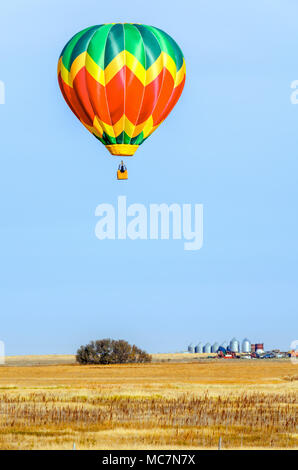 Bunte Ballons mit einem Korb schwebt über dem gelben Feld an einem Sommertag, Traktor, LKW, Wald, Bauernhof und Metal Korn Scheunen im Hintergrund Stockfoto