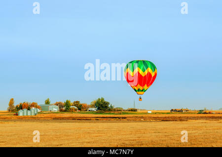 Bunte Ballons mit einem Korb schwebt über dem gelben Feld an einem Sommertag, Traktor, LKW, Wald, Bauernhof und Metal Korn Scheunen im Hintergrund Stockfoto