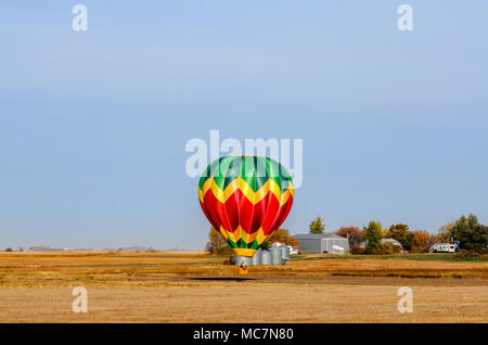 Ein bunter Ballon mit einem Korb schwebt über dem gelben Feld an einem Sommertag, ein Traktor, ein Lkw, einen Wald, einen Bauernhof und Metal Korn Scheunen im Hinterg Stockfoto