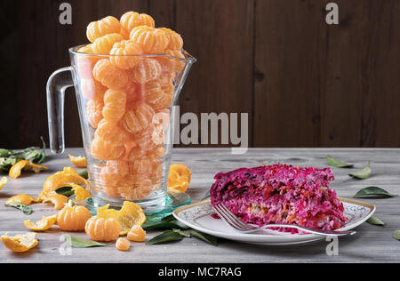 Geschälte frische Mandarinen in Glas Kanne und traditionellen russischen Neues Jahr Salat 'Hering unter einem Pelzmantel". 2-in-1-Salat mit Gemüse und Hering. Stockfoto