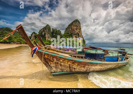 Farbenfrohen traditionellen thailändischen Longtail Boote mit Bändern verziert. Tropischen Sandstrand mit Kalkstein und bewölkter Himmel im Hintergrund. Thailand. Stockfoto