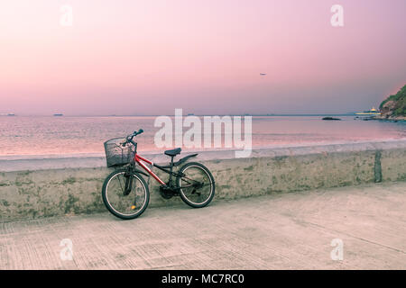 Lonely Fahrrad mit Metall Korb stehend auf betonpfeiler. Seascape Hintergrund mit Fischerbooten auf der Horizontlinie. Getönten Bild. Stockfoto