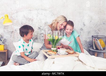 Muttertag - Kinder Überraschung ihre Mutter mit einem Frühstück im modernen Bett Stockfoto