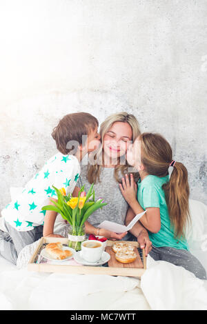 Muttertag - Kinder Überraschung ihre Mutter mit einem Frühstück im modernen Bett Stockfoto