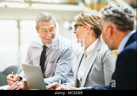 Drei reifen Geschäftsleute lächelnd und zusammen sprechen während einer Sitzung an einem Tisch in einem modernen Büro Stockfoto