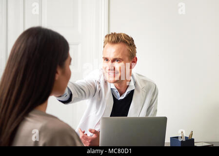 Professionellen Kosmetikerin Mann am Laptop im Büro zu sitzen und das Berühren Frau Gesicht, während Ihr Consulting. Stockfoto