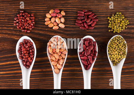 Verschiedenen Hülsenfrüchten in Löffel auf hölzernen Tisch von oben. Gesunde Ernährung Konzept. Stockfoto