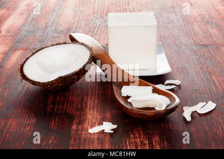Gesund Kokosöl für die Haare. Kokosraspeln in Löffel auf Holztisch. Harte Kokosöl Cube. Stockfoto