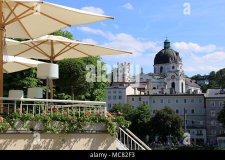 Schönes Cafe mit offenem Sonnenschirme auf der Terrasse begrüßt seine Gäste vor der Stiftskirche (kollegienkirche) in Salzburg, Österreich Stockfoto