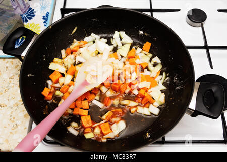 Die Röstung fein gehackte Zwiebeln und Karotten in der Pfanne. Stockfoto