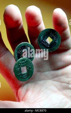 I Ching drei chinesischen I Ching Münzen von einem männlichen Hand geworfen werden. Die Münzen werden verwendet, um einen Numerologischen Herangehensweise an den Text des I Ching zu schaffen Stockfoto
