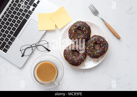 Essen im Büro. Donuts auf Schreibtisch. Stockfoto