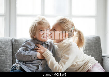 Ältere Schwester umarmen wenig jüngeren Bruder zu Hause, Kind Mädchen küssen Süß schüchtern lächelnd Vorschule junge auf Wange, glückliche Kinder sich gemeinsam amüsiert, l Stockfoto