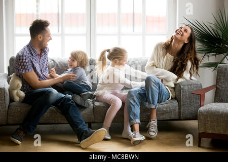 Glückliche Eltern und Kinder, die Spaß kitzeln sitzen zusammen auf dem Sofa, freundliche Paar lachen Spiel mit wenig aktive Kinder Sohn und Daughte Stockfoto