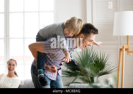 Glücklich, Vati, die kleinen niedlichen Kind Junge auf, zurück zu geben Kind piggyback ride Spaß zusammen haben zu Hause, freundliche Vater spielen mit aufgeregt Vorschule Stockfoto