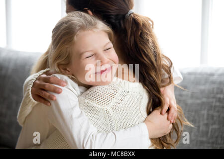 Süße kleine Tochter umarmen Mutter dichtholen, Mom und glücklich, Kindergarten oder Schule Mädchen Kuscheln, ein Lächeln auf den Lippen Aufrichtiges Kind umarmen Mumie, warme Relati Stockfoto