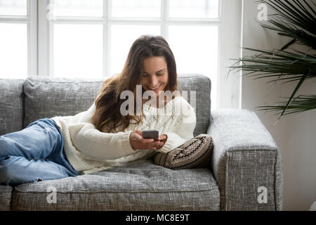 Glückliche junge Frau auf Sofa mit Smartphone home liegend, lächelnd Teen Girl holding Handy genießen das Chatten mit Freunden oder neuen Mobile Apps, Text Stockfoto