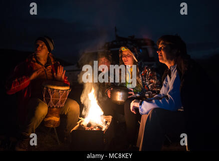 Vier Freunde sitzen in der Nähe der Feuer, Spielen am Schlagzeug und genießen ihre lagerleben an der Natur. Stockfoto