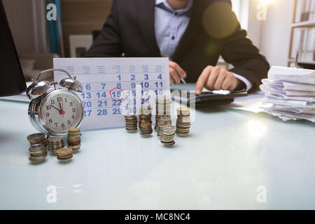 Close-up Gestapelte Münzen und Kalender Neben dem Unternehmer Hand mit Taschenrechner Stockfoto