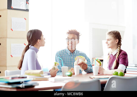 Gruppe der befreundeten Studenten sitzen, Schreibtisch und dem Mittagessen bei Bruch zwischen Klassen Stockfoto