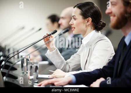 Ein junger Politiker sprechen in das Mikrofon unter den anderen Teilnehmern der Konferenz Stockfoto