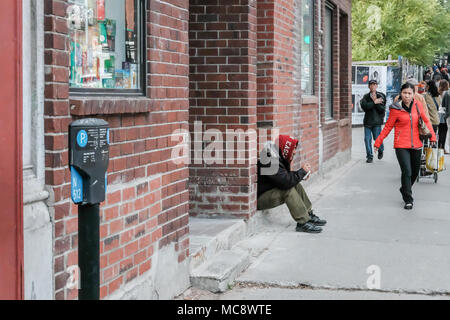 Obdachlose erwachsene Männchen gesehen, für Nächstenliebe, während innerhalb einer Tür in einer geschäftigen Nordamerika Straße sitzen, während Menschen, die auf dem Bürgersteig. Stockfoto