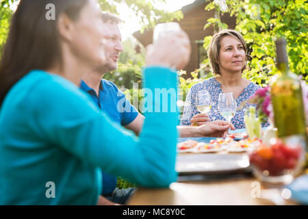 Freunde versammelten sich um einen Tisch im Garten einen Sommer am Abend eine Mahlzeit zu teilen und gemeinsam Spaß haben. Stockfoto