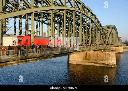 Ein Lokbespannte Zug überquert die Hohenzollernbrücke in Köln, Deutschland Richtung Osten als Fußgänger auf einem sonnigen Sonntag zu Fuß Stockfoto