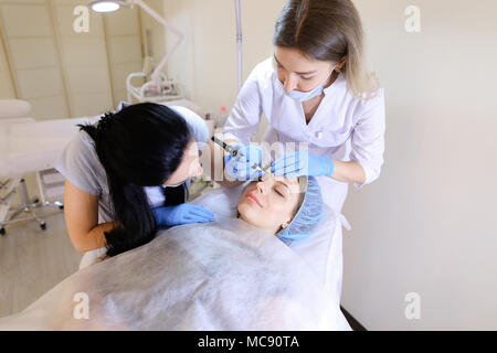 Blond Kosmetikerin Permanent Make-up für die Frau am Schrank mit der Krankenschwester. Stockfoto