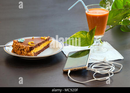 Köstliche Schokolade Kuchen und Smartphone mit Eistee Glas- oder Orangensaft im Coffee Shop in der Tabelle verschwommenen Hintergrund. Stockfoto