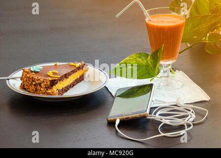 Köstliche Schokolade Kuchen und Smartphone mit Eistee Glas- oder Orangensaft im Coffee Shop in der Tabelle verschwommenen Hintergrund. Stockfoto