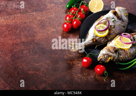 Gebackene gegrillte Fisch, Dorado, Dorade mit Zitrone, Kräuter, Gemüse und Gewürze auf rustikalen Hintergrund gekocht. Ansicht von oben. Kopieren Sie Platz. Stockfoto