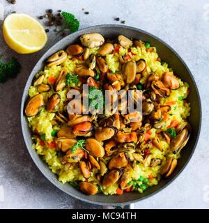 Traditionelle spanische Paella in der Pfanne Reis, Erbsen, Krabben, Muscheln, Tintenfisch auf Hellgrau konkreten Hintergrund. Ansicht von oben, Copyspace. Stockfoto