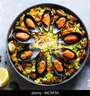 Traditionelle spanische Paella in der Pfanne Reis, Erbsen, Krabben, Muscheln, Tintenfisch auf Hellgrau konkreten Hintergrund. Ansicht von oben, Copyspace. Stockfoto